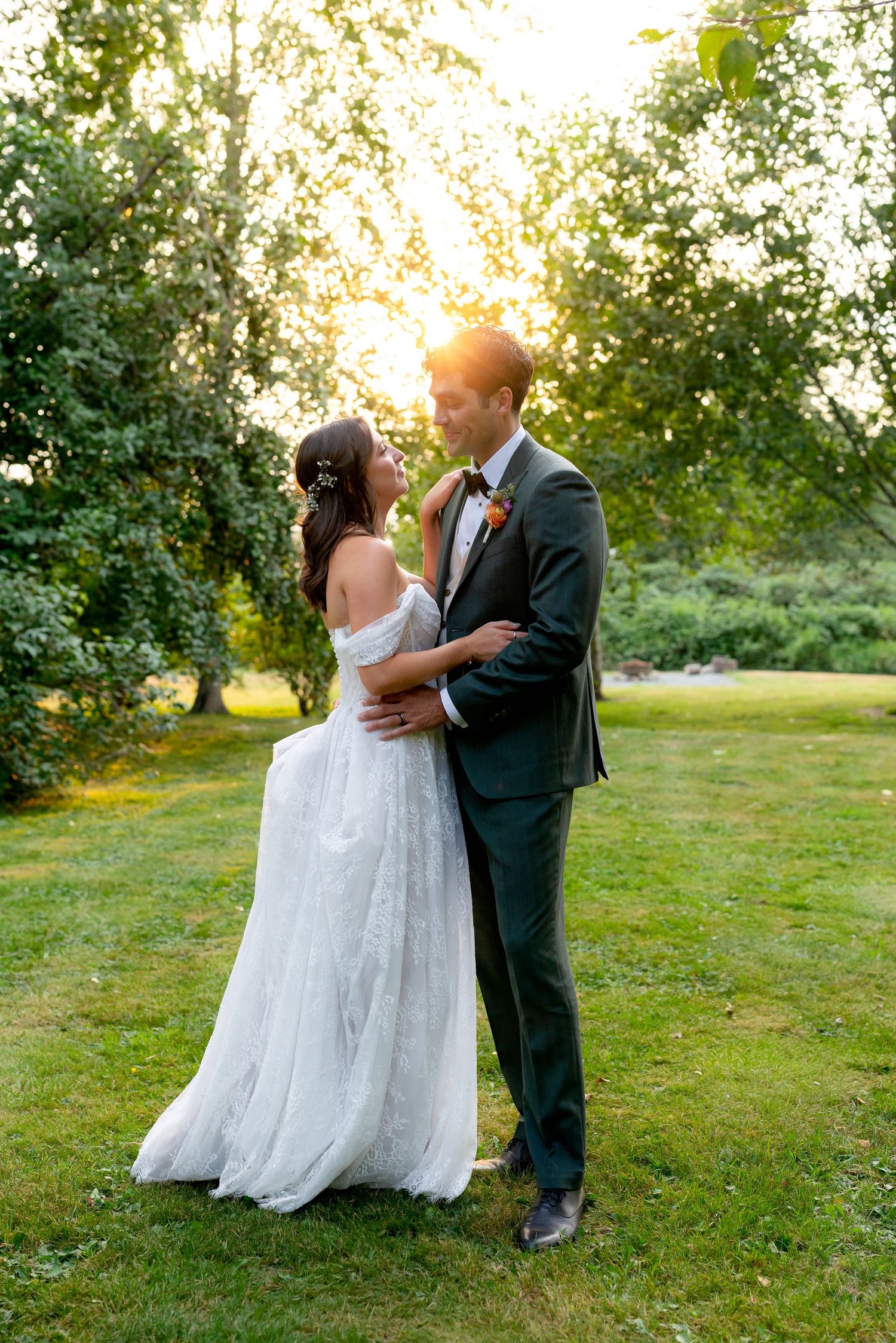 Bride and groom embrace at golden hour in a lush garden, bride in off-shoulder gown, groom in dark suit.