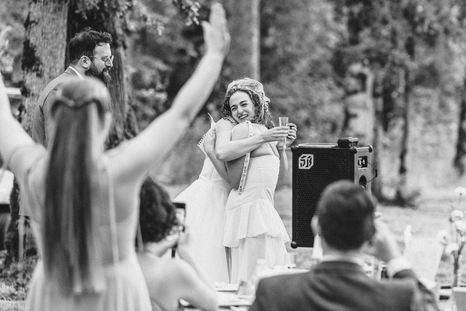 Wedding guests dancing and celebrating at an outdoor reception surrounded by trees and natural scenery.