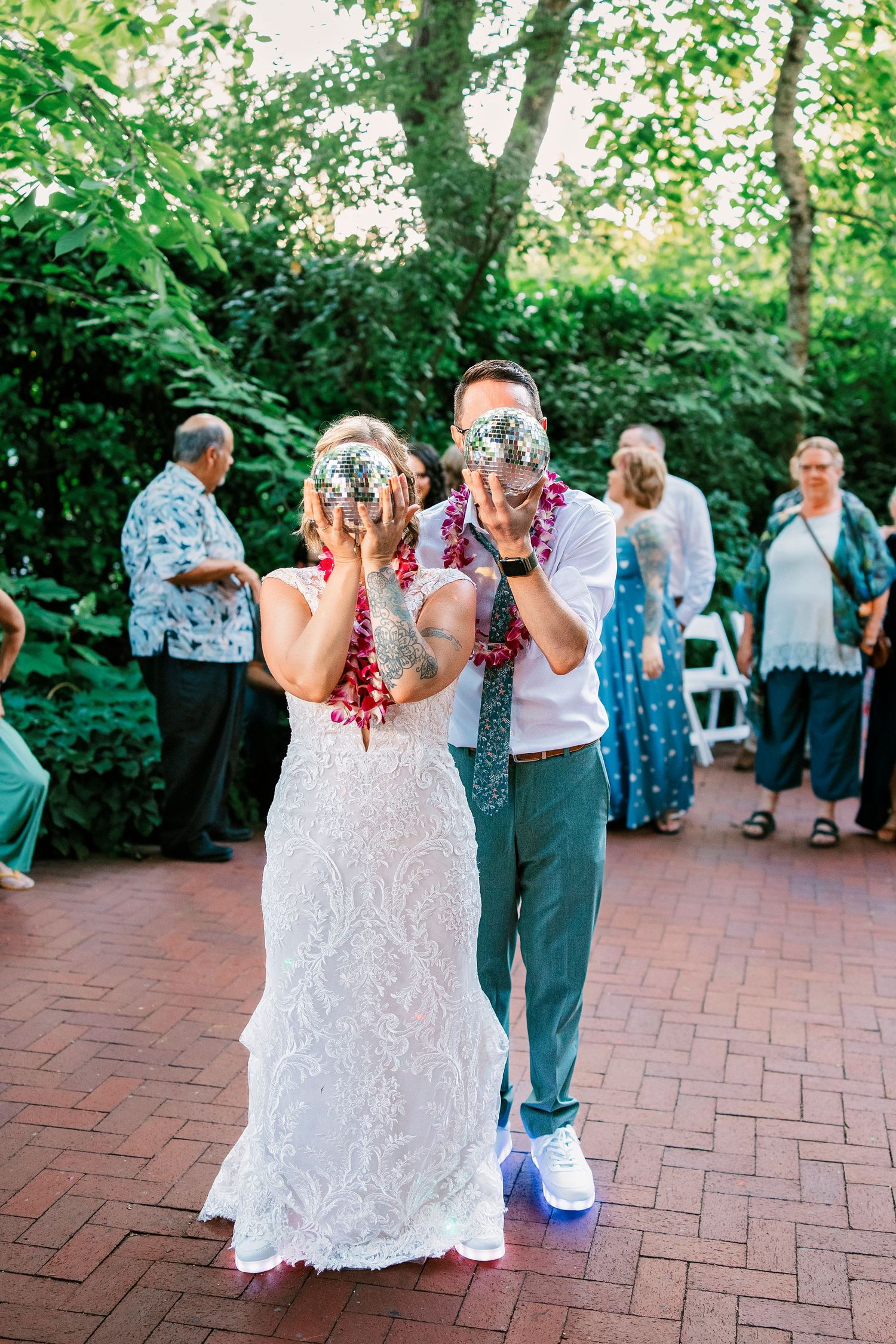 Wedding guests dance together on a brick patio surrounded by lush greenery.