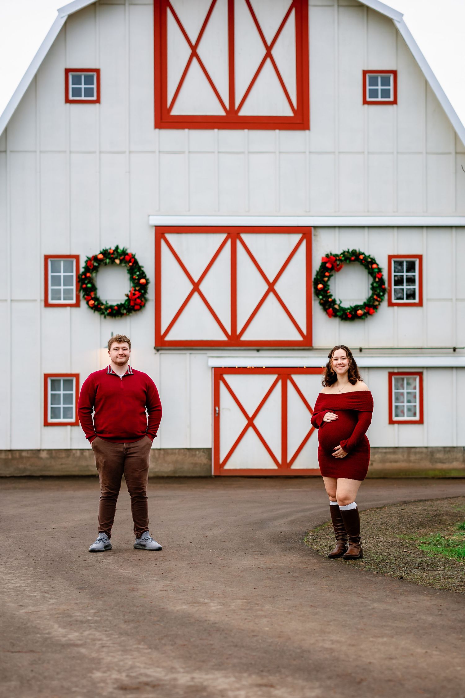 A festive white barn with red trim and Christmas wreaths creates a charming holiday backdrop.