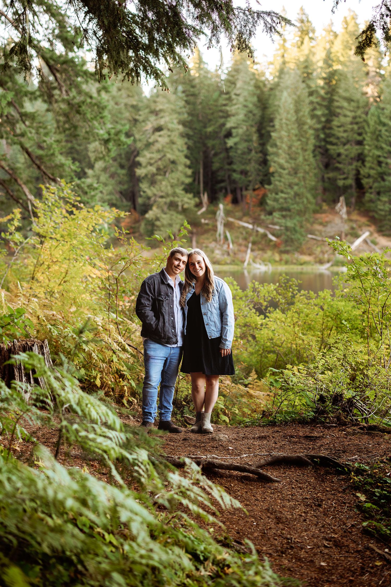 Couple walking through a scenic forest trail with ferns and evergreens.