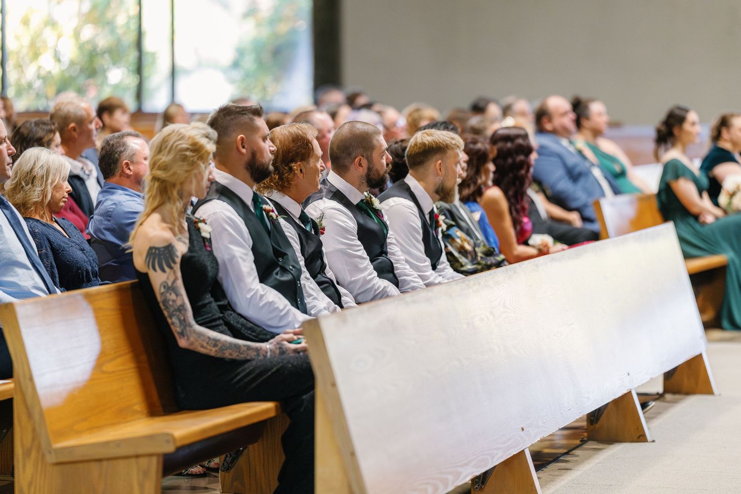 Wedding guests fill rows of wooden pews in a church sanctuary during a ceremony.