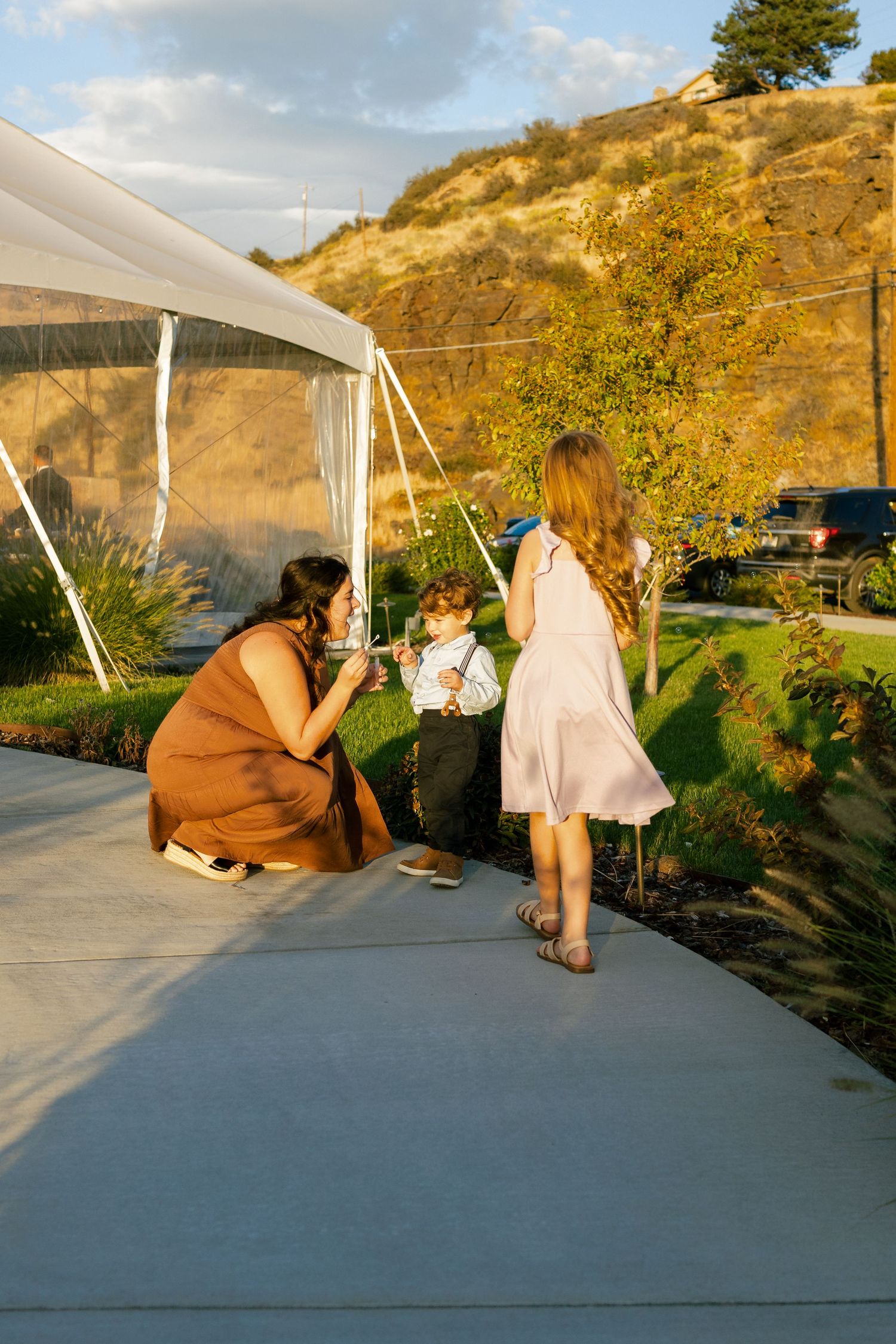 People relaxing on a concrete patio with golden hills and mountains in the background at sunset.