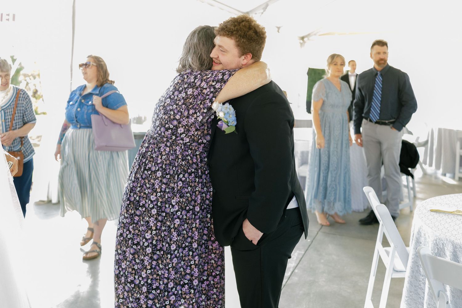 Wedding reception guests mingle in an airy white venue space with natural lighting.