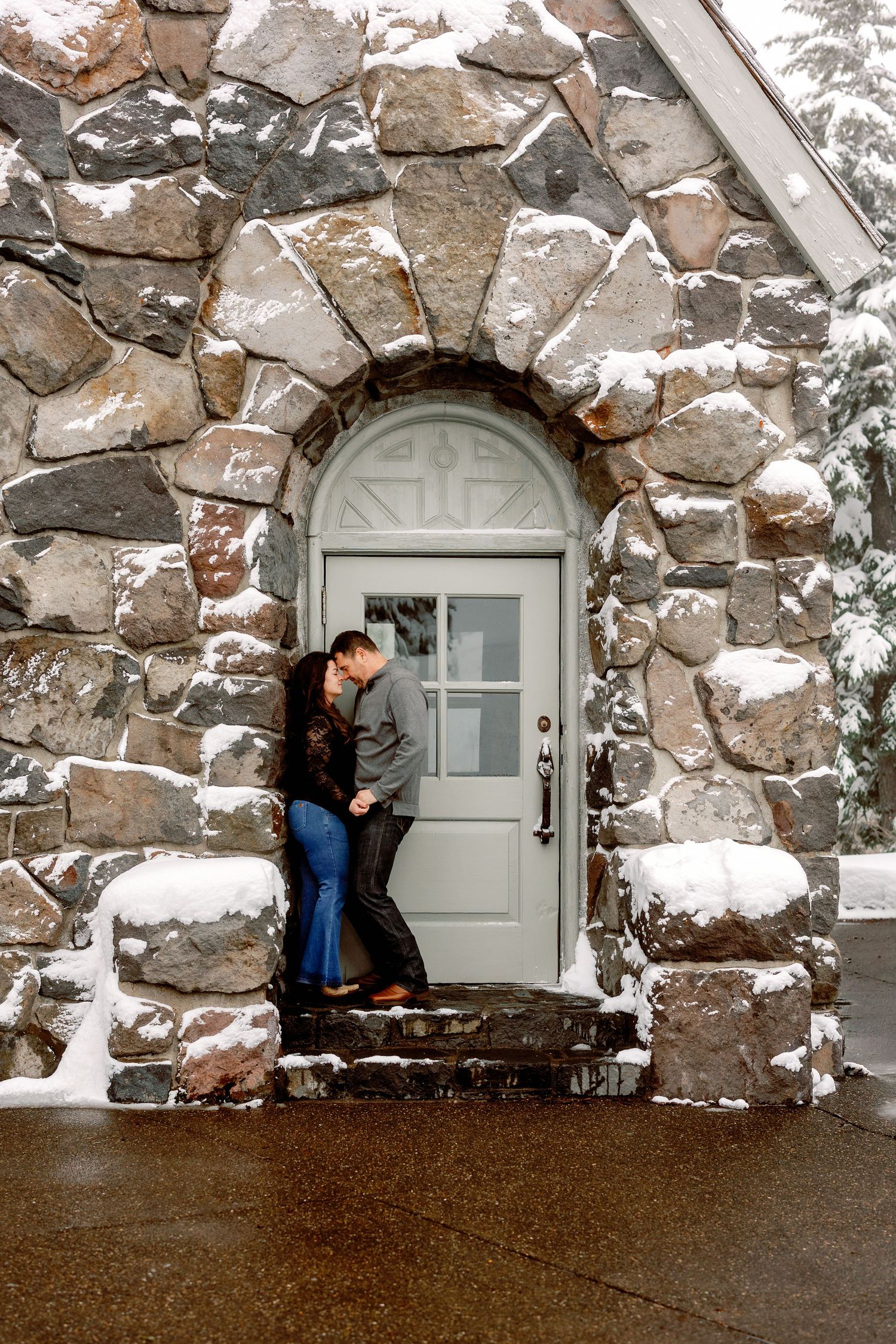 A couple shares an intimate moment in a snow-covered stone archway entrance during winter.