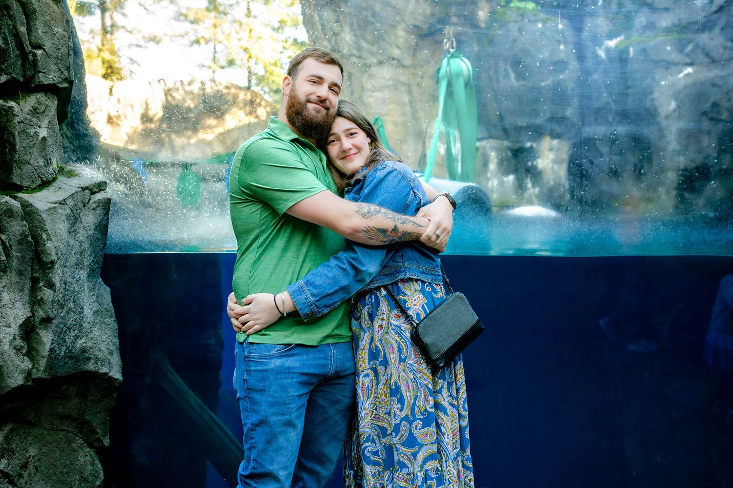 A couple shares a tender moment while viewing an exhibit at what appears to be an aquarium or zoo.