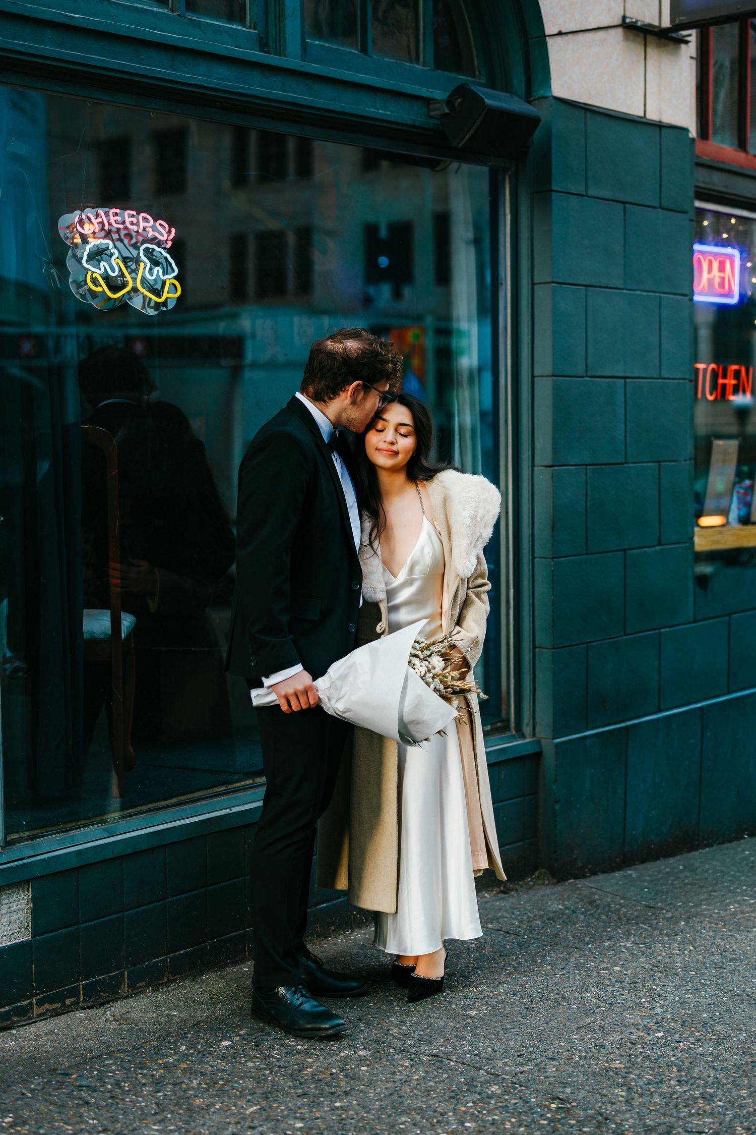 A couple embraces outside a storefront with teal-colored walls.