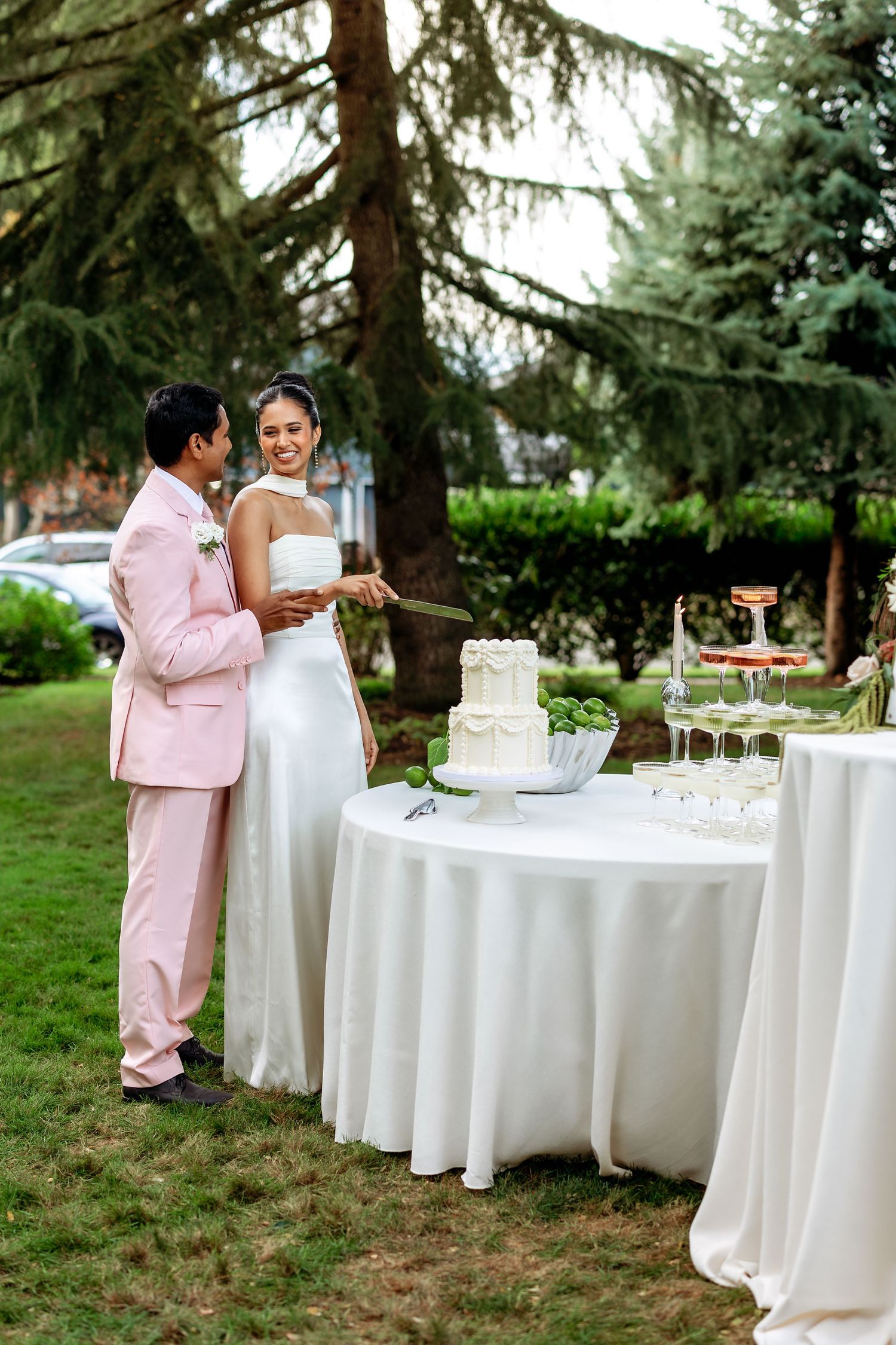 Wedding reception setup with white-clothed tables under evergreen trees.