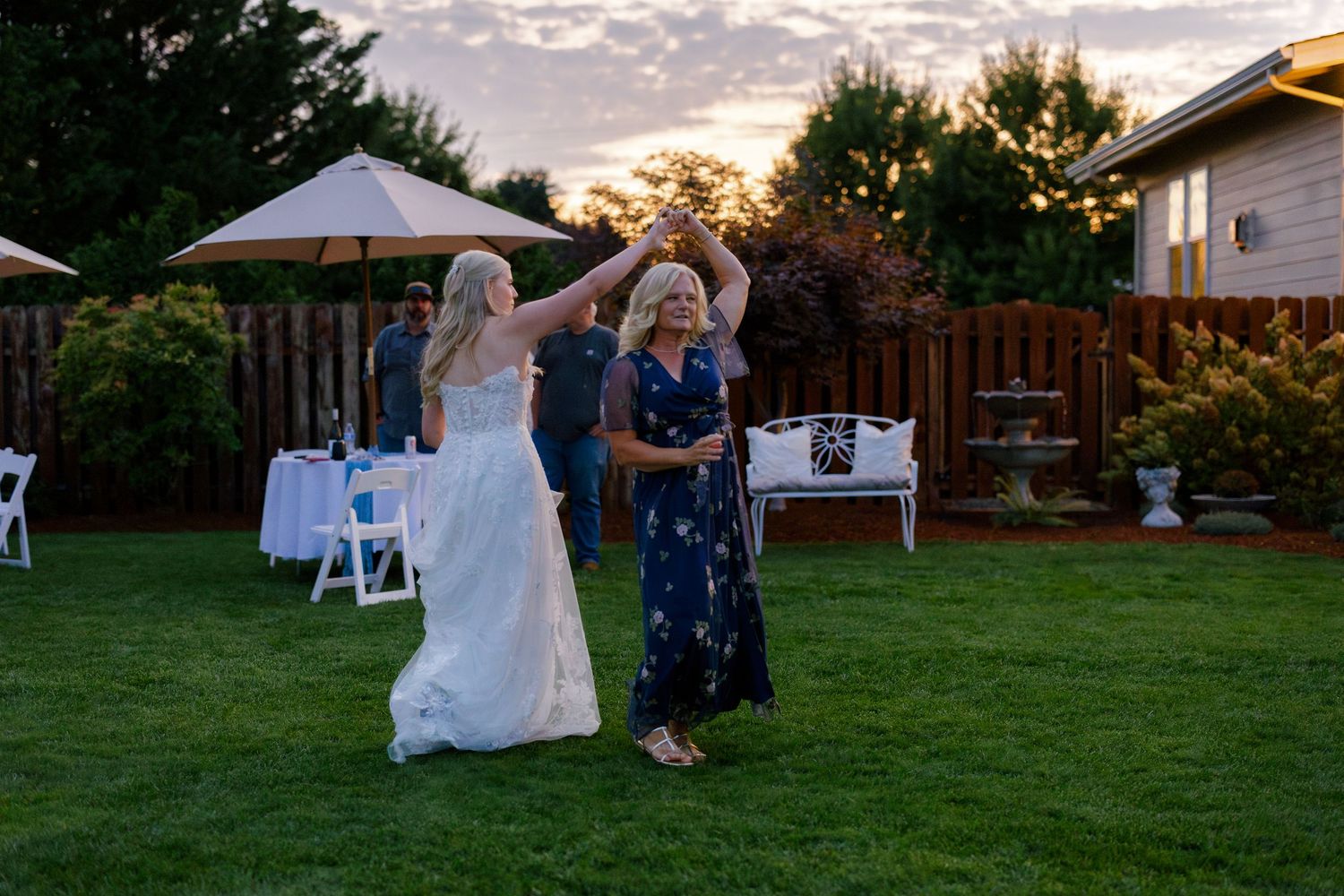 Wedding celebration in a backyard garden during golden hour with dancing and white chairs.