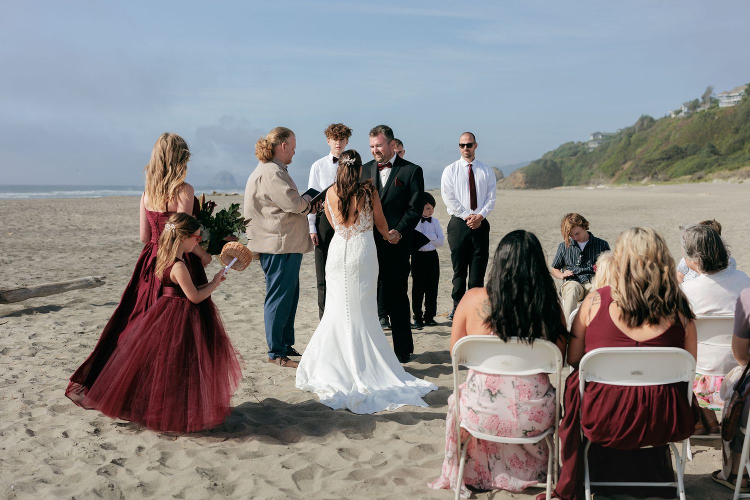 Beach wedding ceremony setup with guests seated on white chairs against an ocean backdrop.