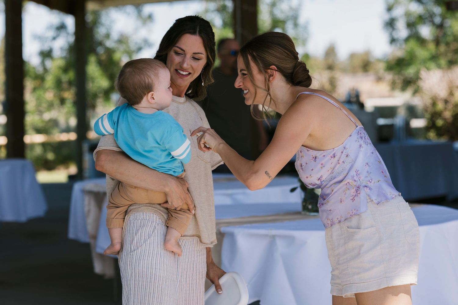 Three people share a joyful moment together at an outdoor event with white tablecloths in the background.