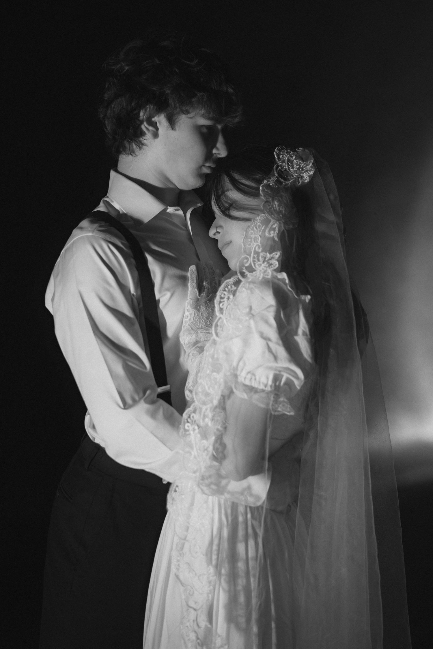 A black and white portrait of a couple in vintage wedding attire embracing in an intimate moment.