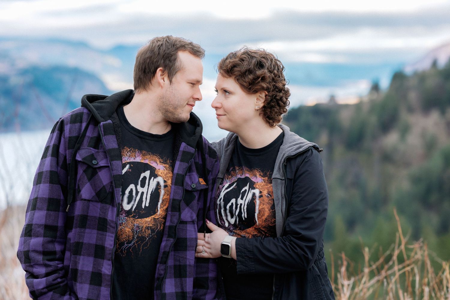 A couple shares tender moments during an outdoor photo session in a mountainous landscape wearing casual clothing.