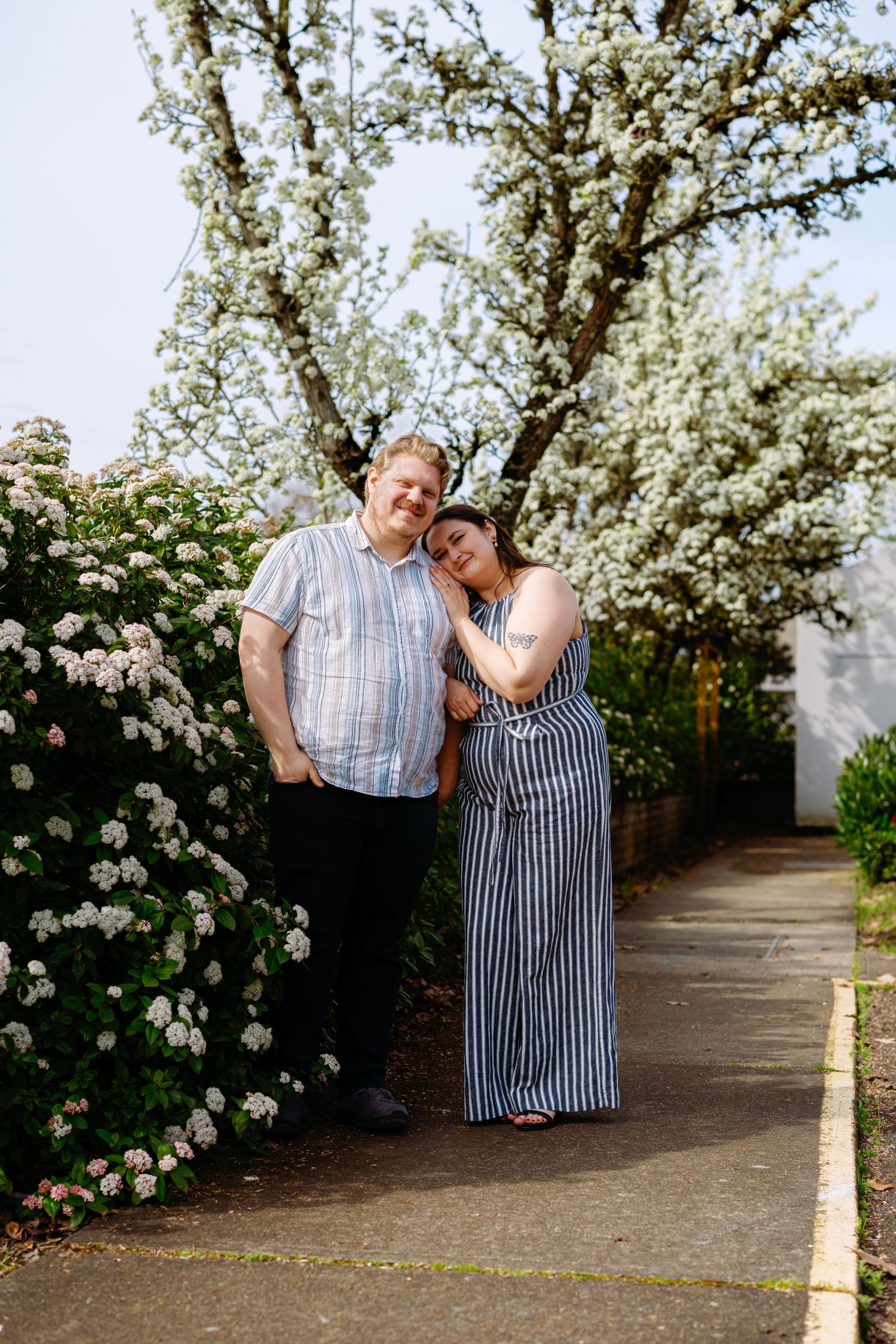 A couple shares a romantic moment among blooming white cherry blossom trees in a garden pathway.