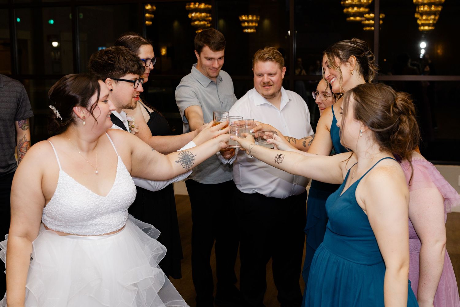 Wedding guests clinking glasses together in celebratory toast on dance floor at indoor reception.