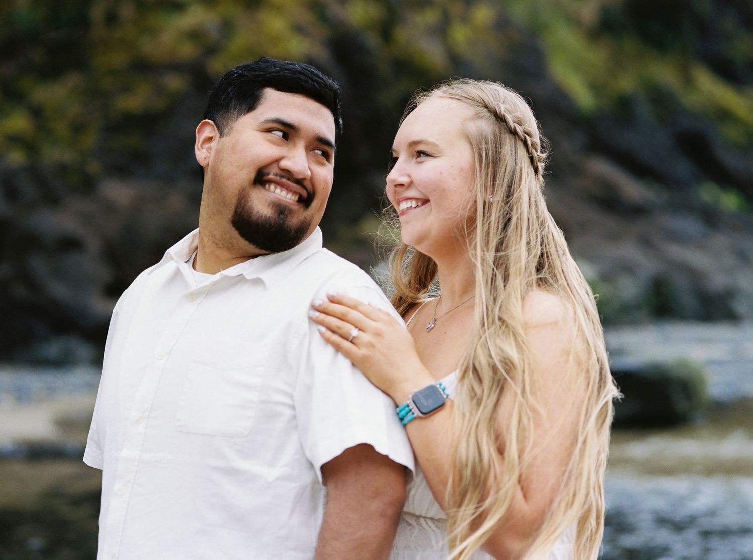 Close-up of smiling couple outdoors, woman in white dress with blue smartwatch, man in white shirt.