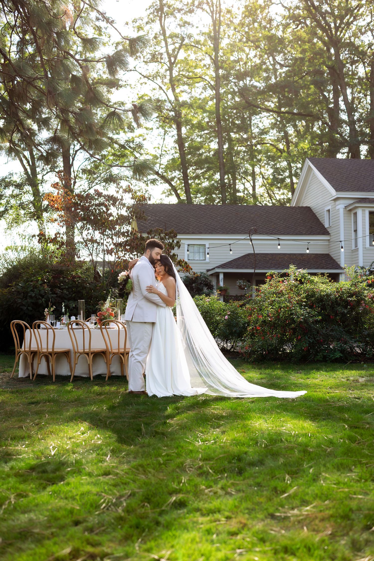 A wedding ceremony setup in a sunlit garden with white chairs and floral arrangements along a grassy aisle.