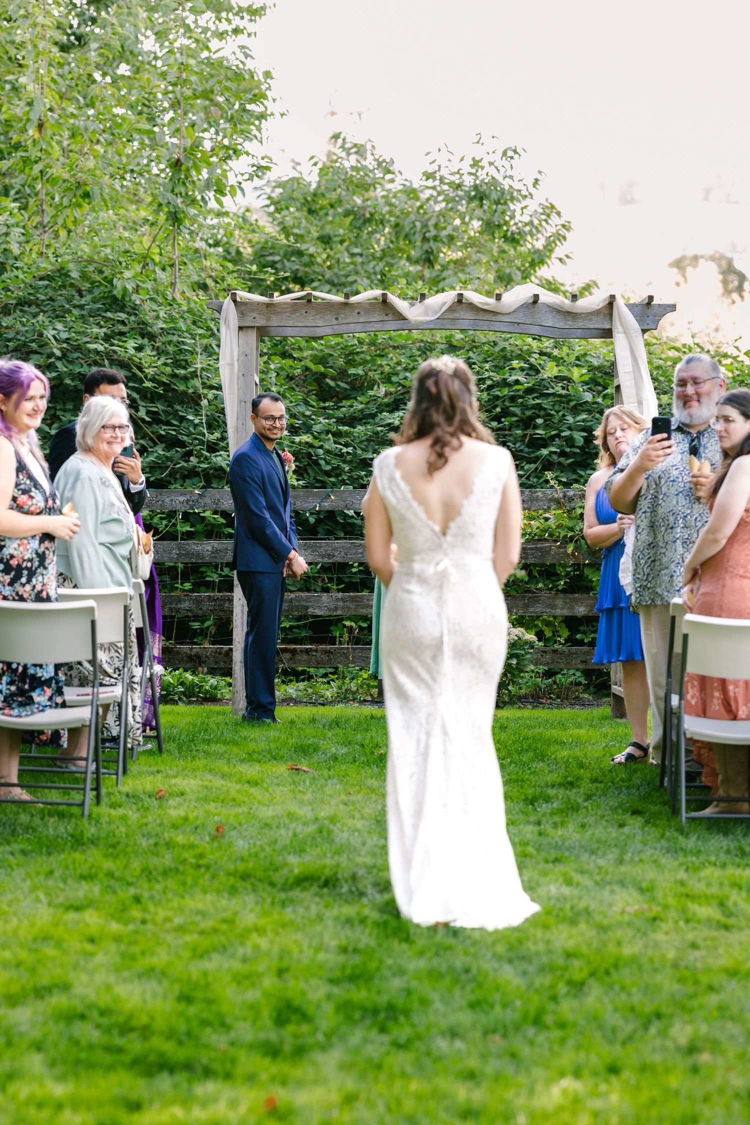 Wedding guests mingle and celebrate at an outdoor garden reception with white decor and green lawn.