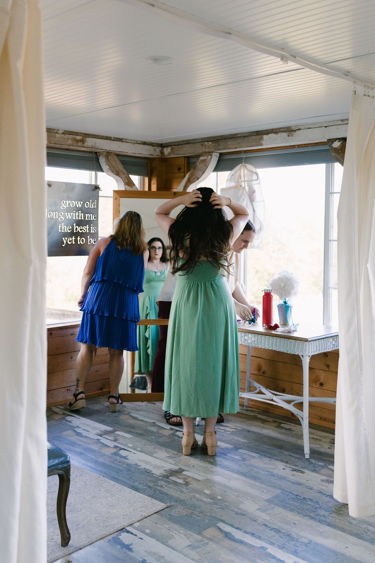 Bridesmaids in blue and mint green dresses explore a rustic white interior space during wedding preparations.