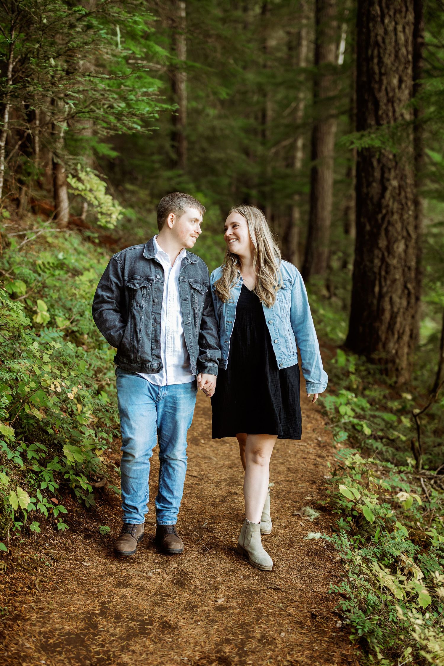 A couple walking together on a forest trail wearing denim and casual attire in natural lighting.