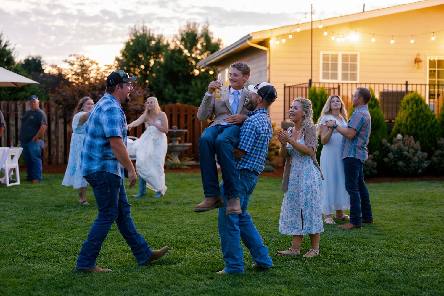 Wedding guests dancing on a lawn at dusk with a yellow house in the background.