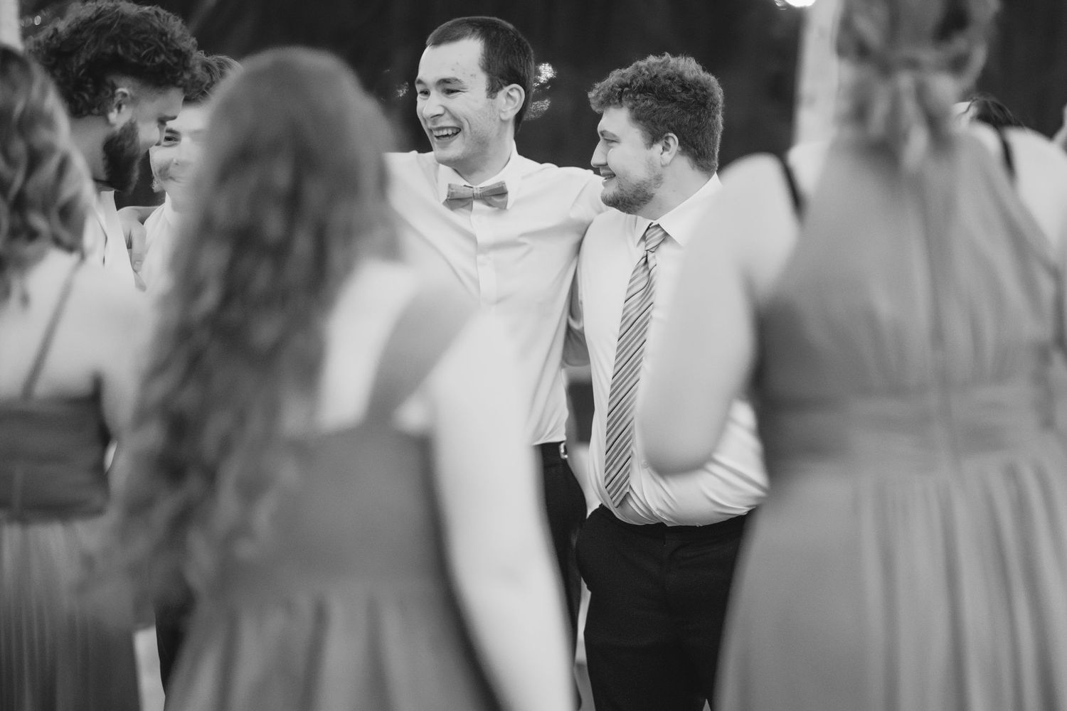A joyful wedding reception dance party with guests celebrating on a wooden dance floor under string lights.