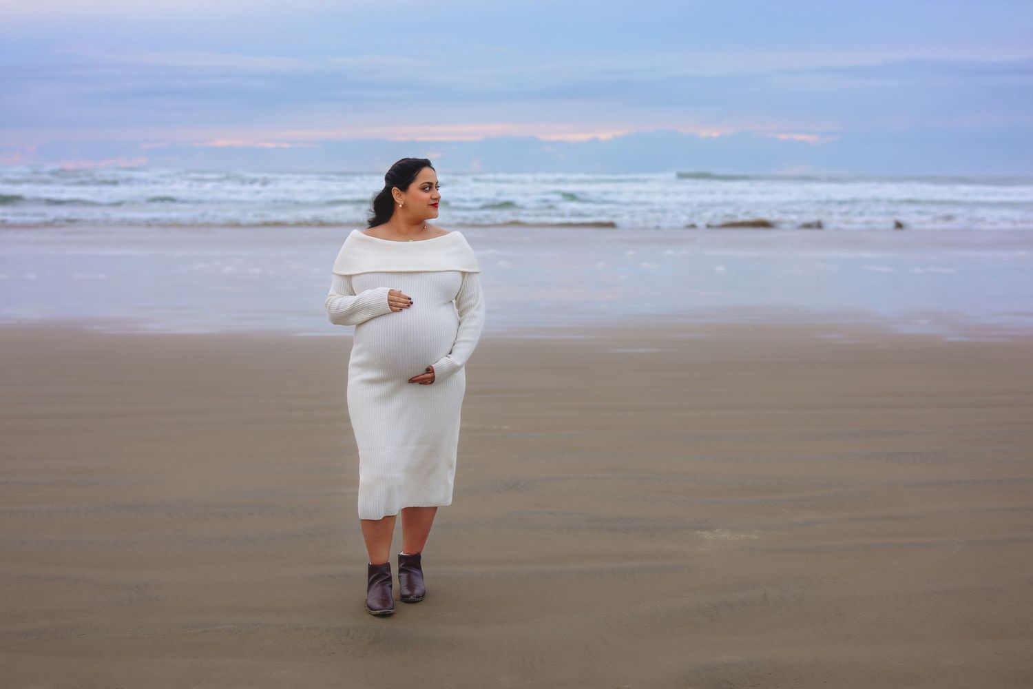 A figure in a white off-shoulder dress stands on a misty beach at sunset wearing purple boots.