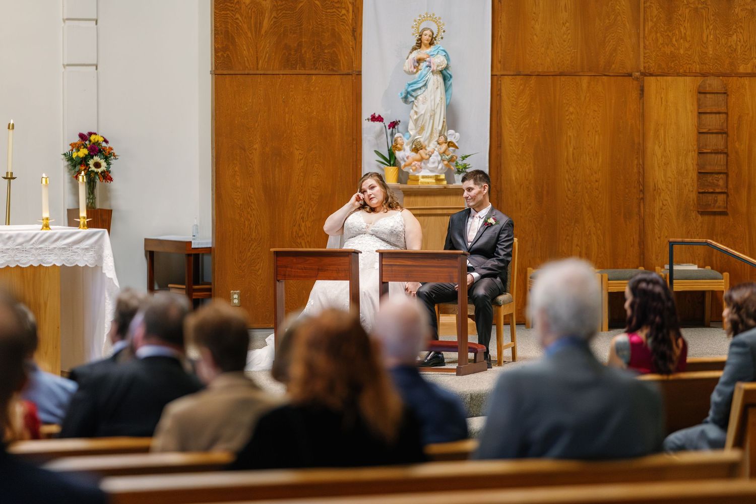 Interior view of church ceremony with wooden paneled walls and guests seated in pews.