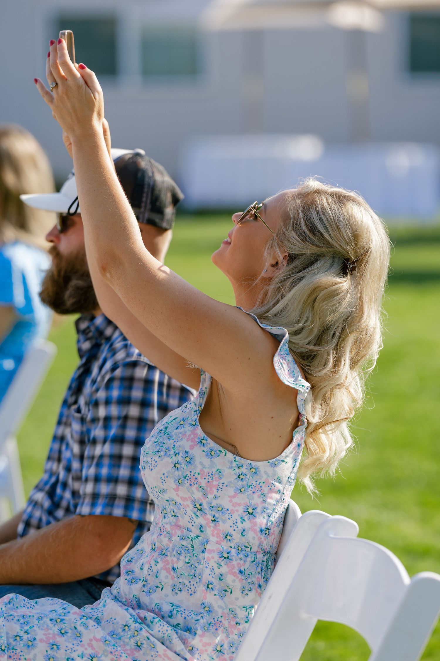 Guest in floral dress taking photo with raised phone during outdoor event.