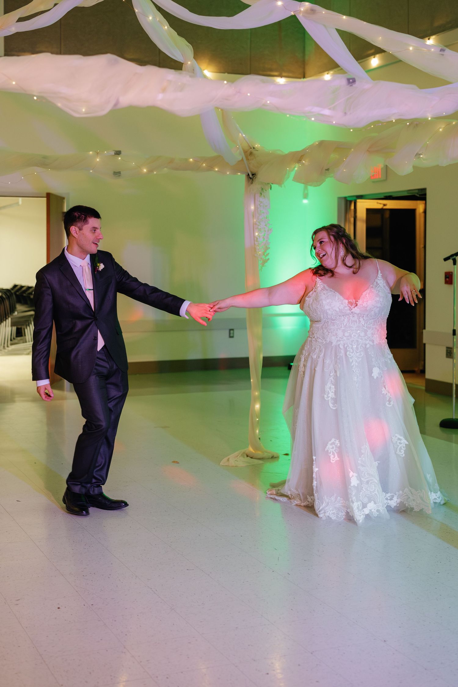 Wedding couple performs their first dance in a ballroom illuminated with pink and green lights.