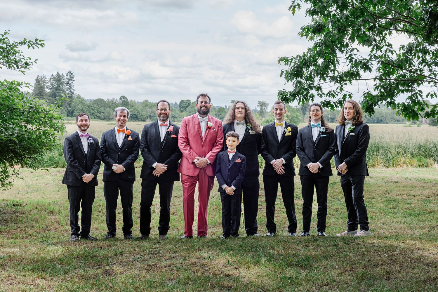 Wedding party poses outdoors with one member wearing a standout red suit among dark suits.