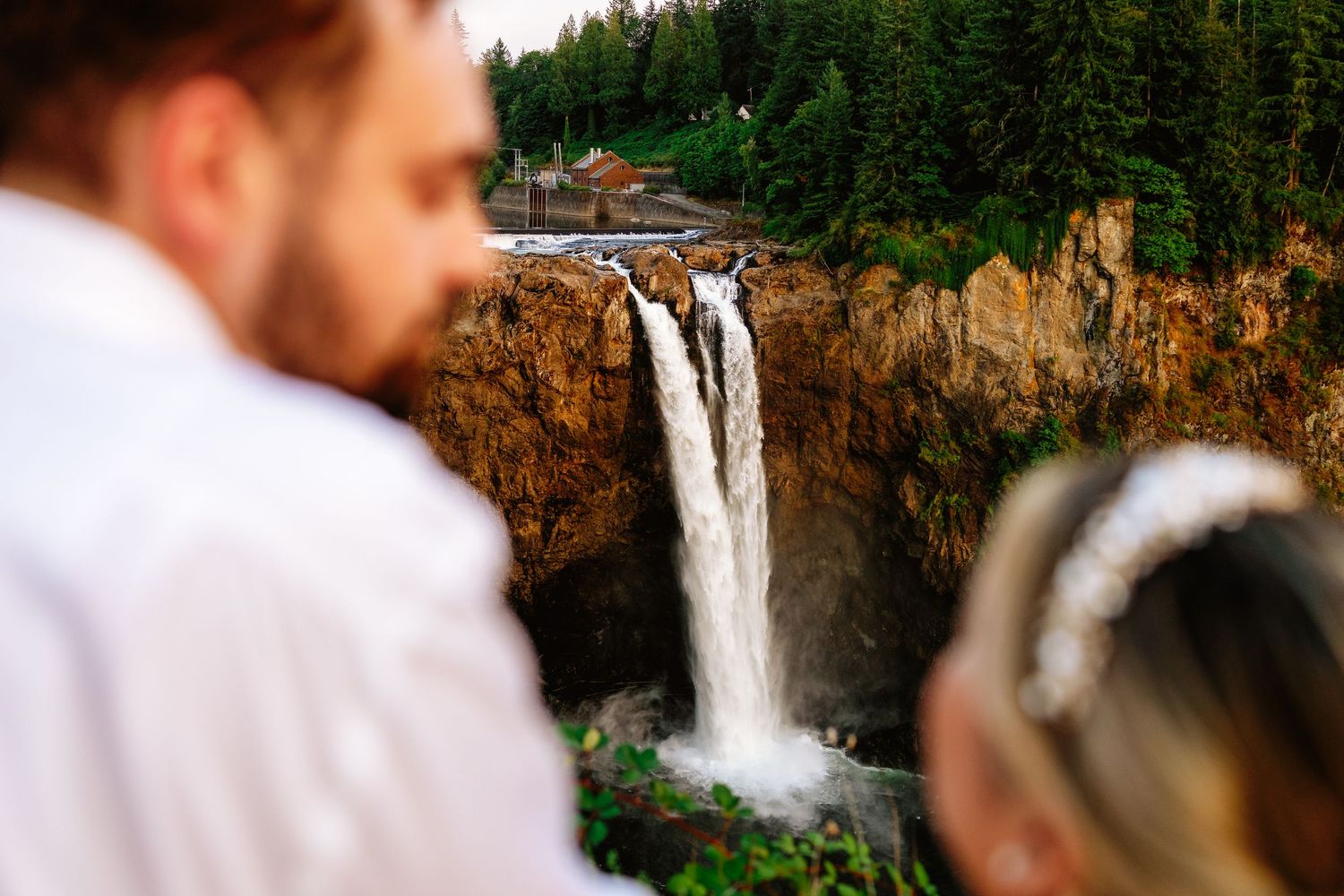 Snoqualmie Falls cascades down rocky cliffs in Washington state as visitors observe from the viewing platform.