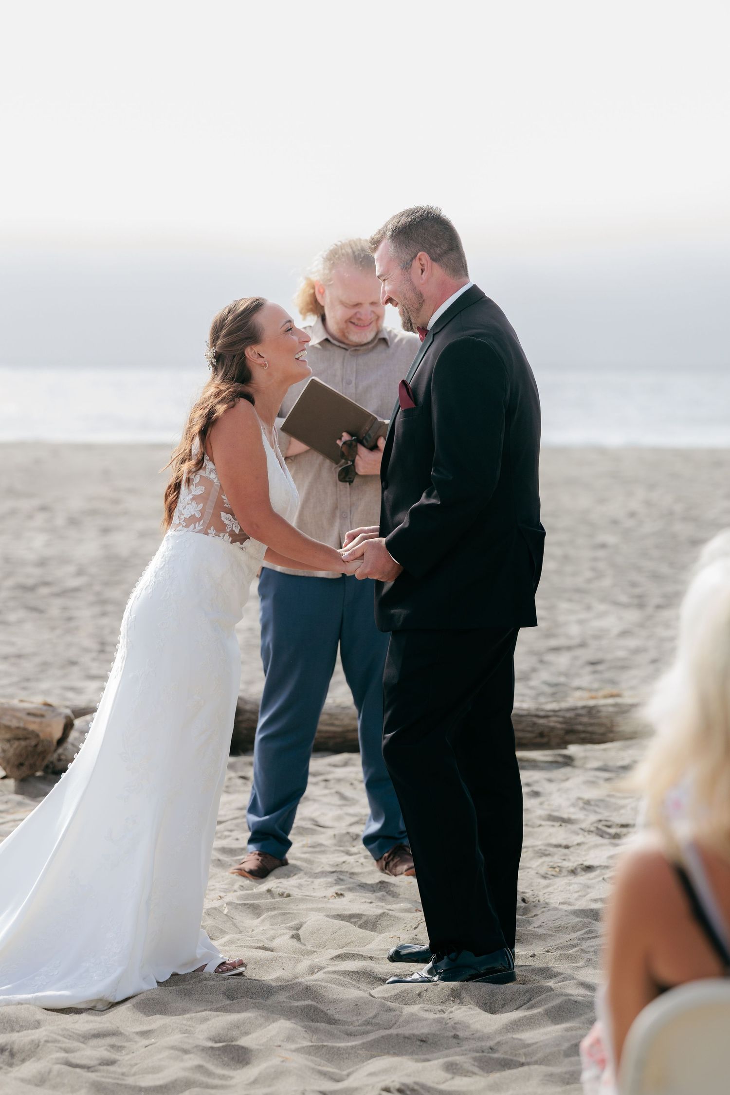 A beach wedding ceremony takes place with the couple and officiant standing together on the sand near the ocean.