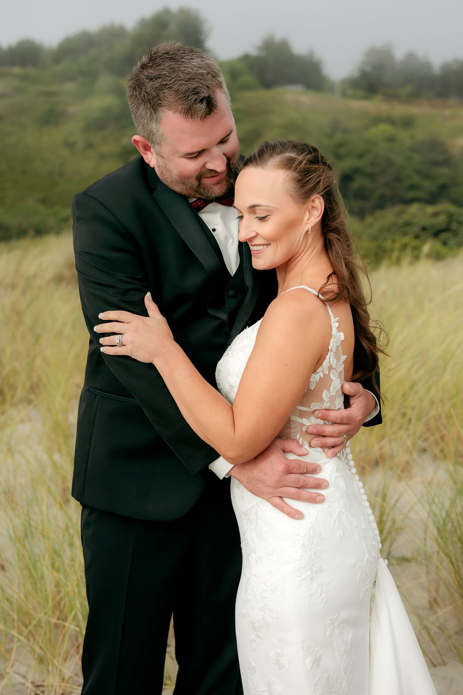 A romantic wedding couple embraces in a field of tall grass during their outdoor photo session.