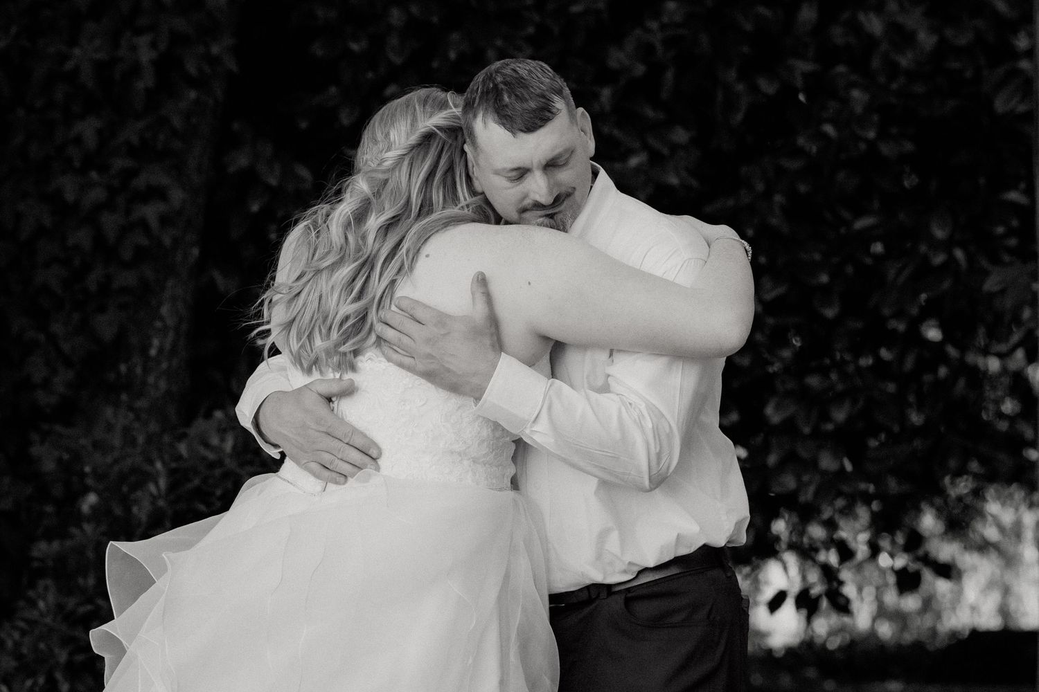 Bride and groom share an emotional embrace in a black and white photo.