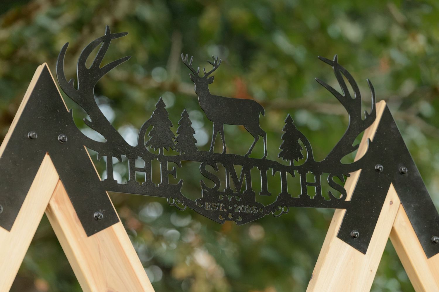 Decorative metal sign reading The Smiths with deer silhouette design mounted on wooden wedding arch.