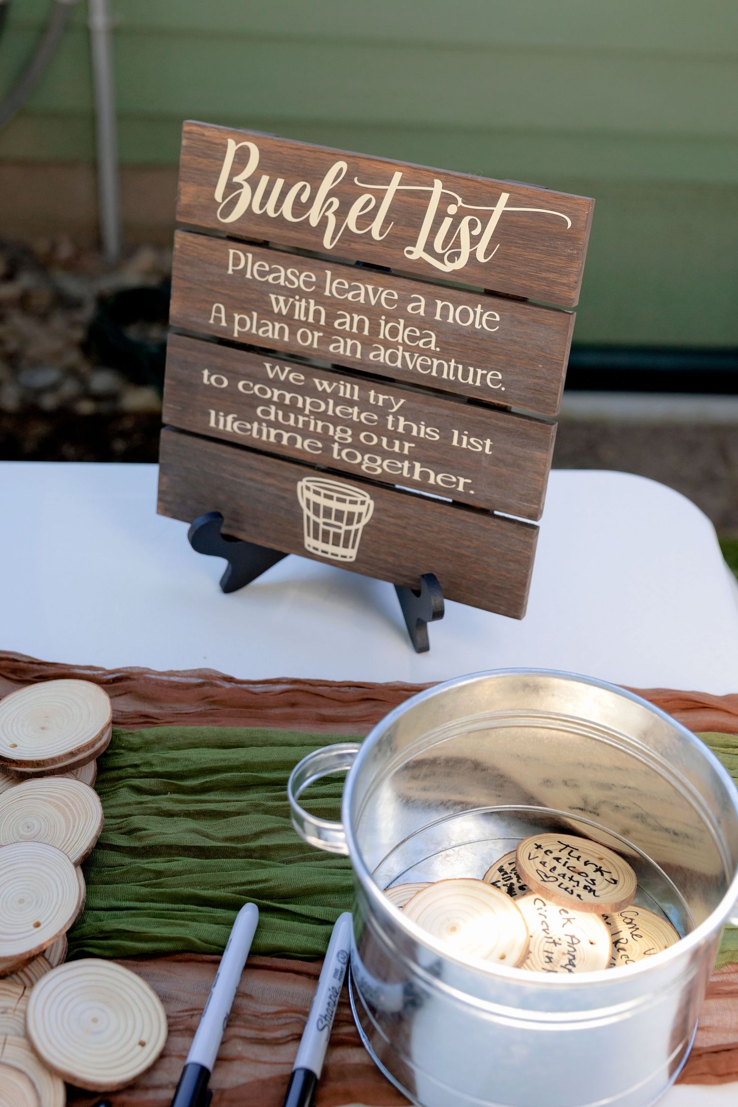 Rustic wooden bucket list wedding guest sign with wood slices and metal pail for notes.