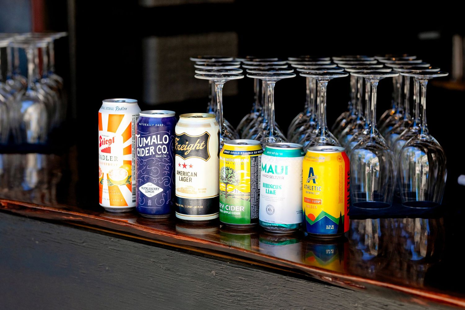 Assorted craft beer cans and wine glasses displayed on a wooden bar counter.