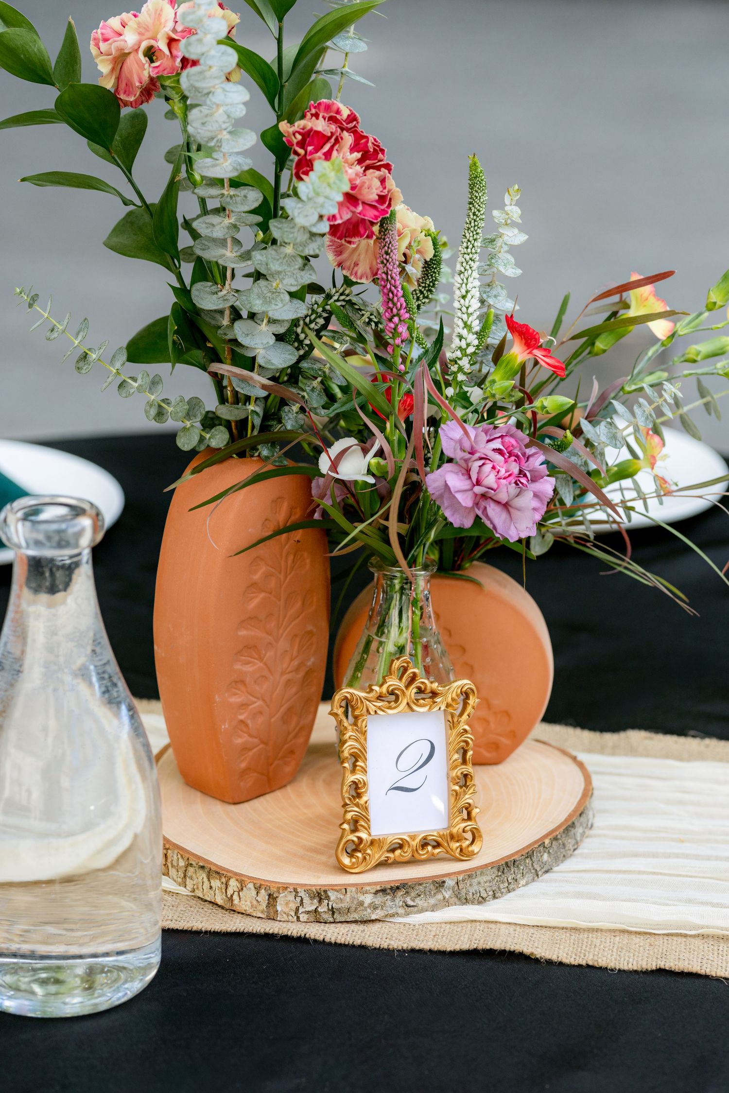 Wedding table centerpiece with colorful flowers in terracotta vase on wood slice.