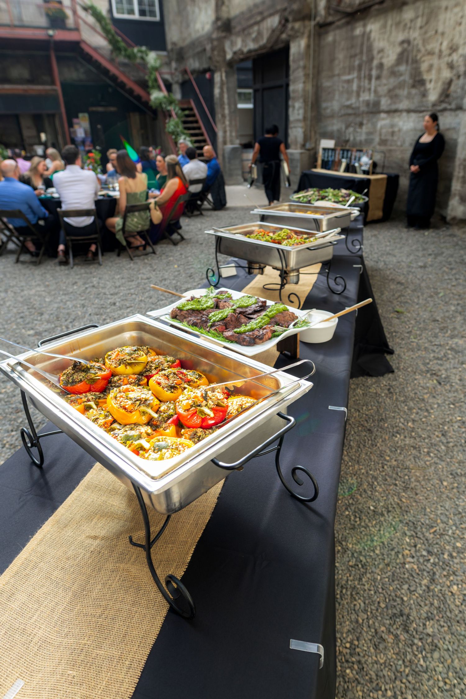 Elegant outdoor wedding buffet with chafing dishes filled with colorful roasted vegetables for guests.