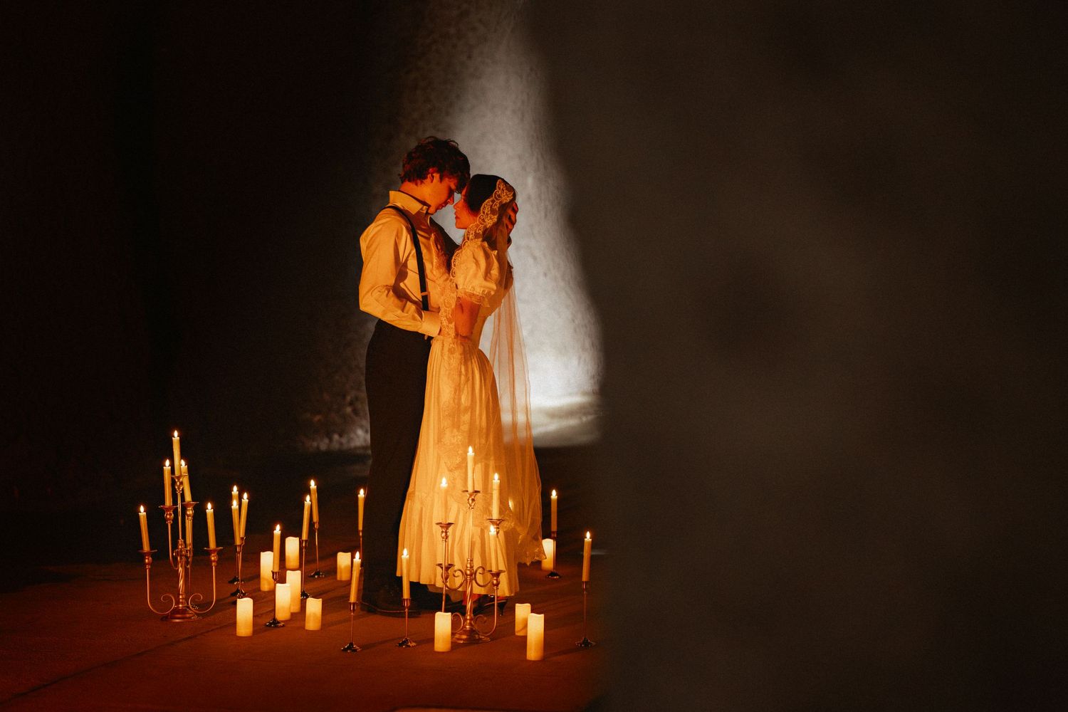 A dramatic scene with figures in orange dress illuminated by candlelight in a dark atmospheric setting.
