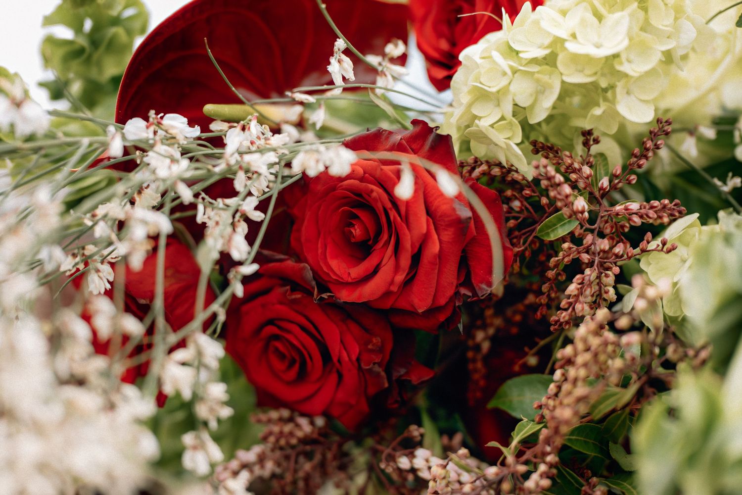 A vibrant wedding bouquet featuring deep red roses and white flowers with delicate greenery and berries.