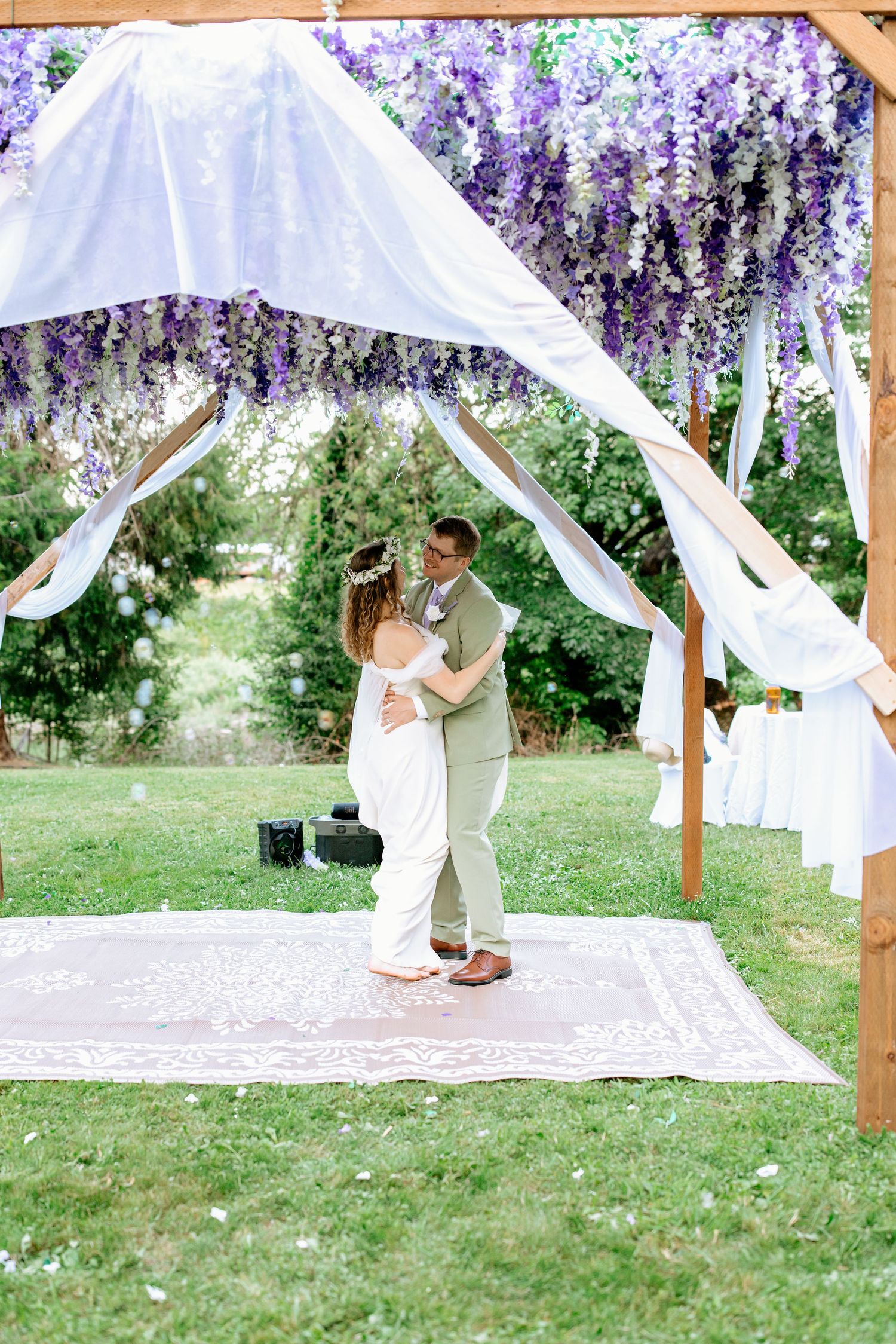 Bride and groom share first dance under a stunning purple wisteria floral wedding arch.
