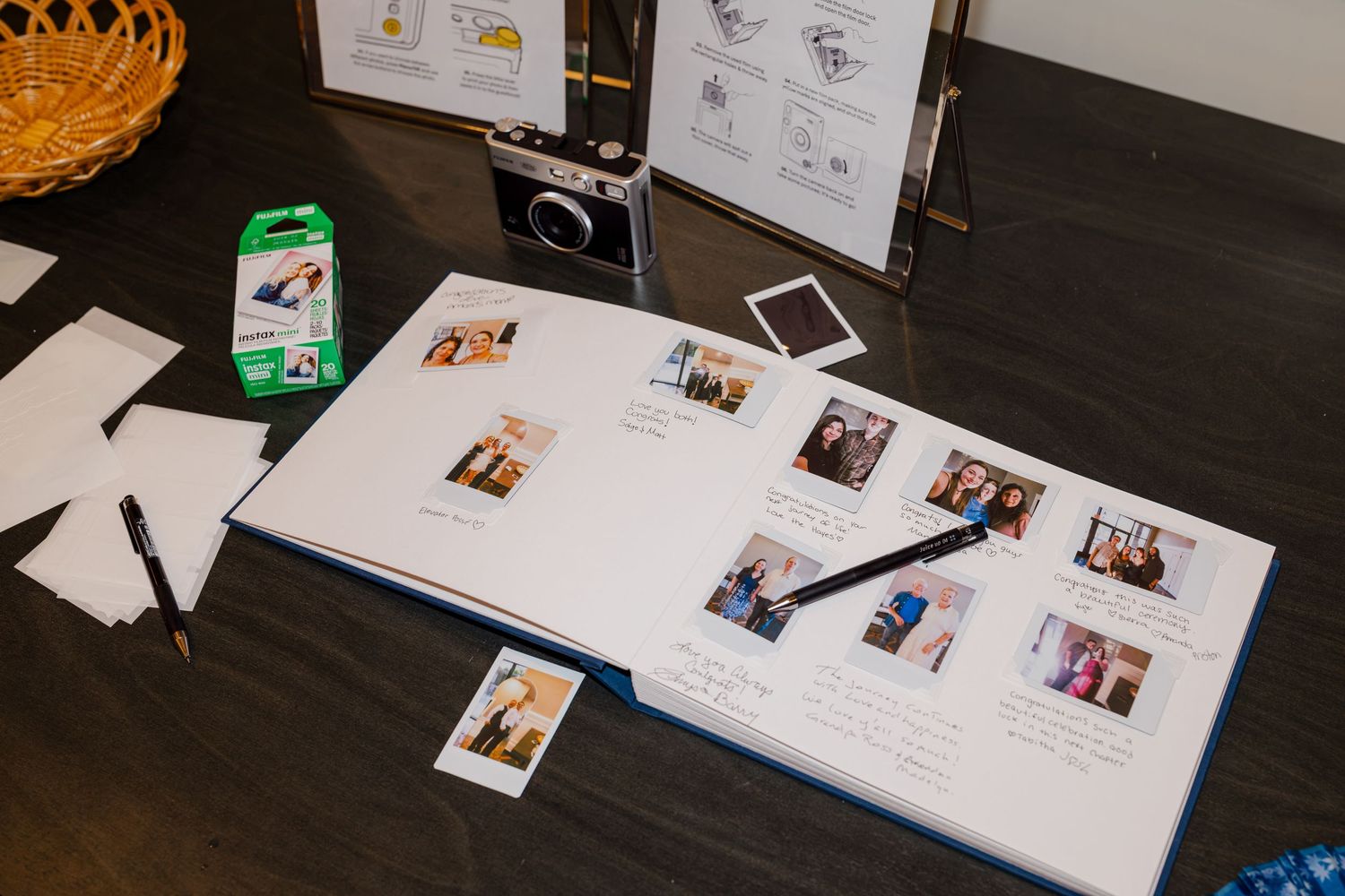 Wedding guest book open with Instax photos and a Fujifilm camera on a wooden table.