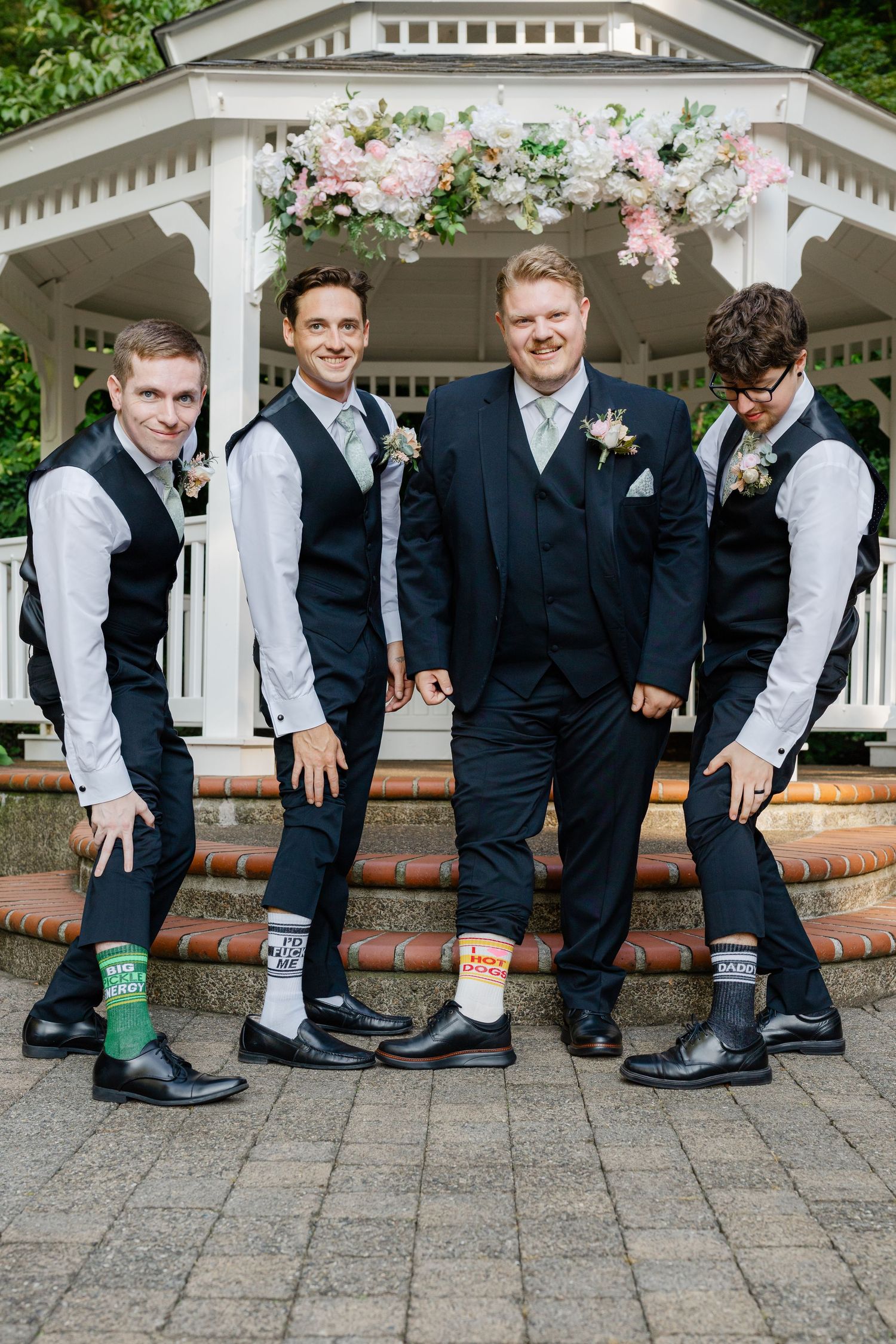 Groom and groomsmen showing off fun patterned socks in front of a floral decorated gazebo.