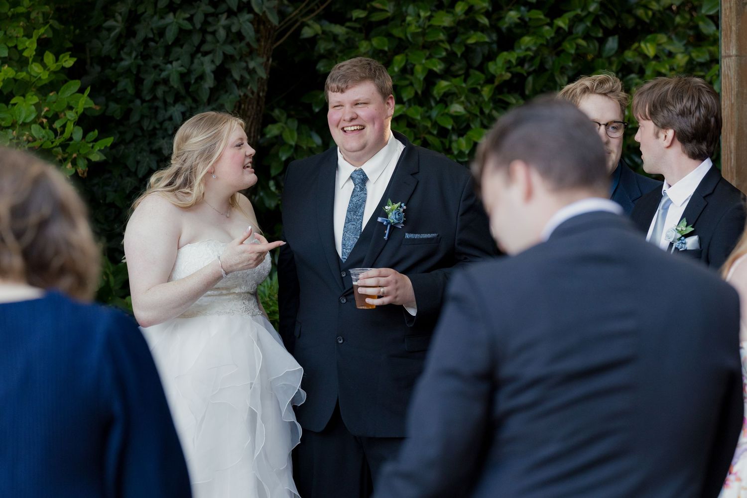 Laughing bride and groom socializing with wedding guests at outdoor reception in garden setting.