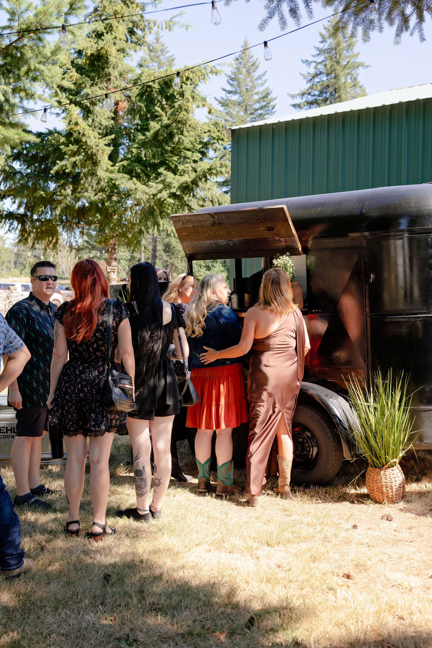 Wedding guests line up at vintage food truck under pine trees at outdoor rustic wedding reception.