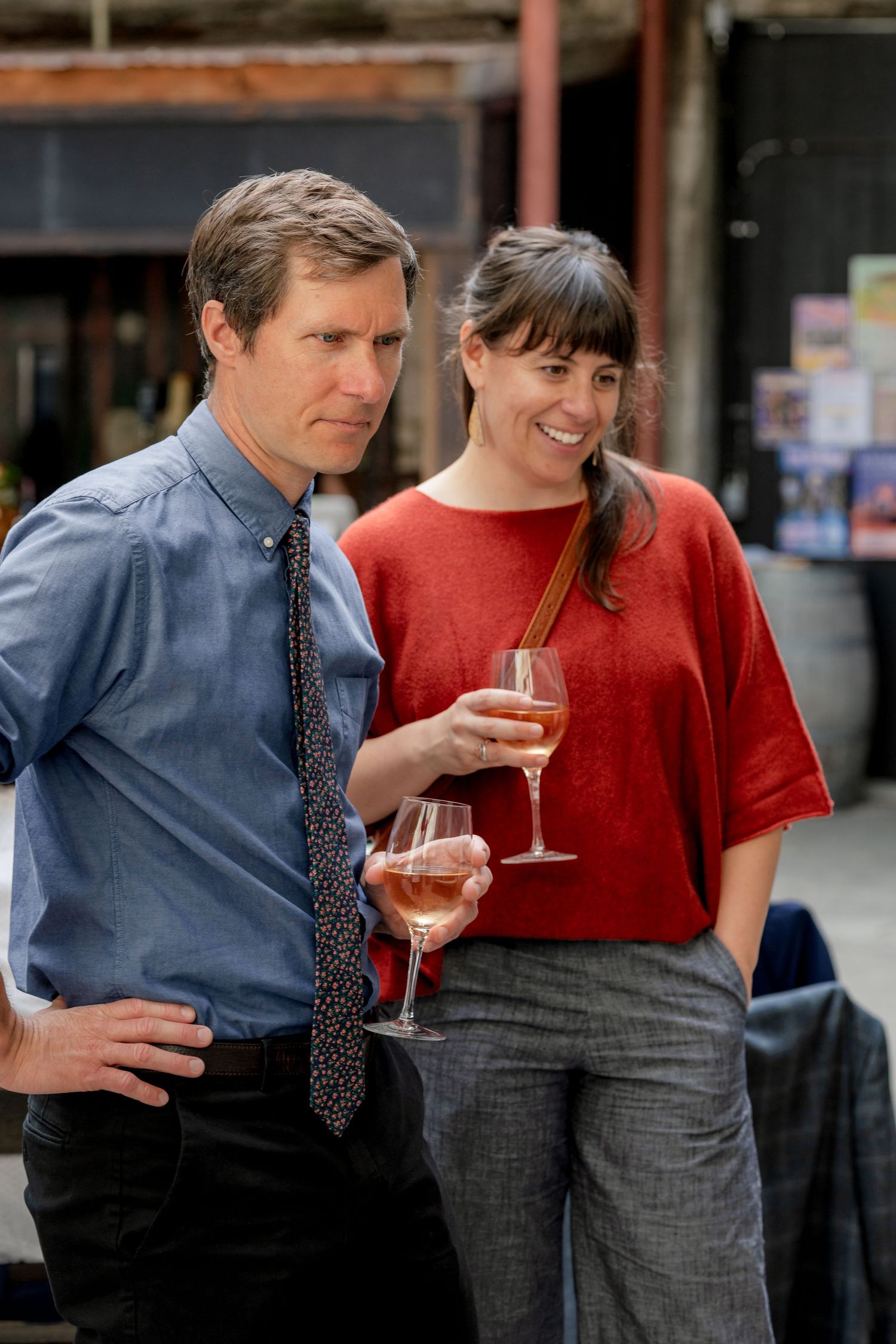 A smiling man and woman holding rose wine glasses chat together at an outdoor wedding reception event.