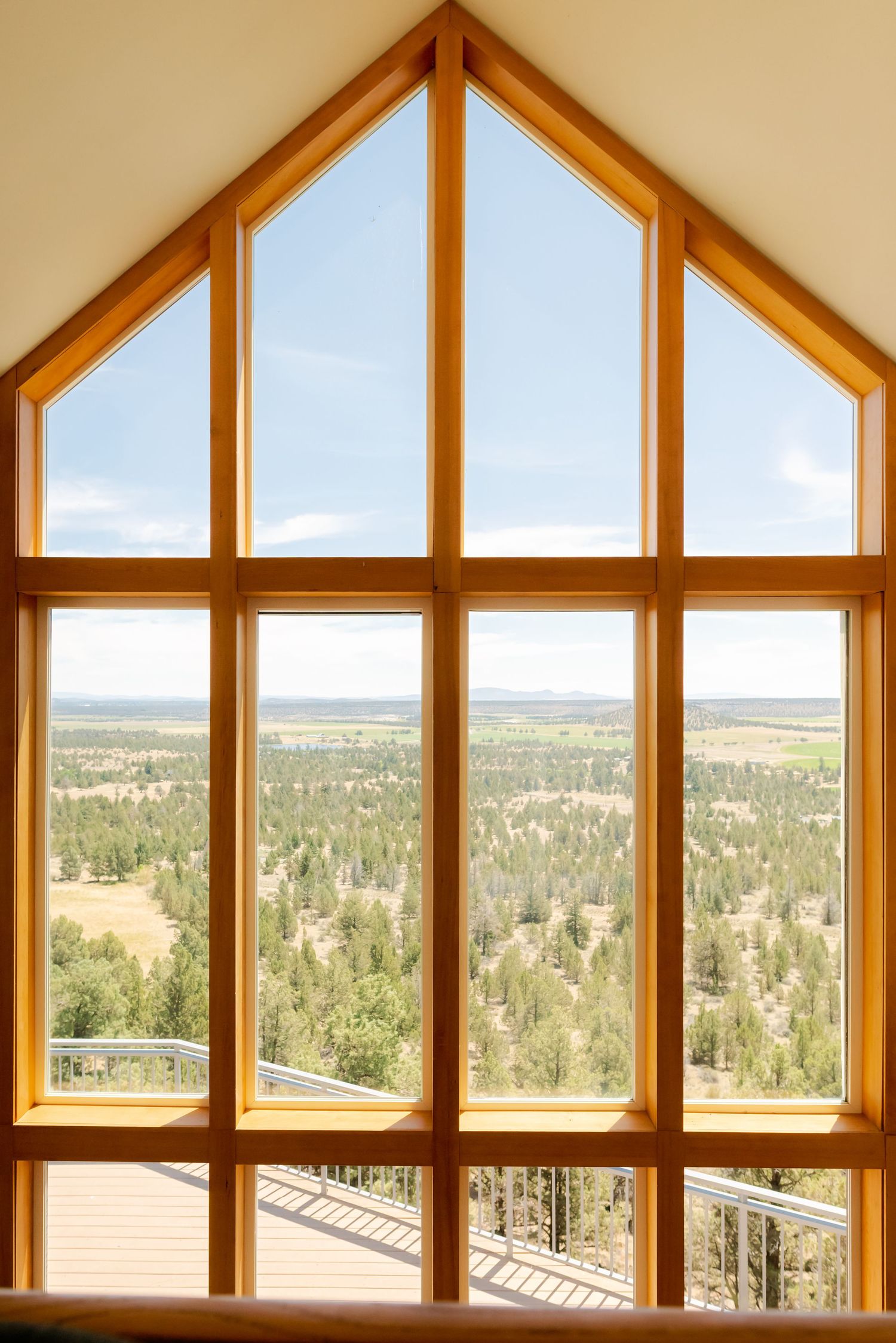 Large wooden-framed gable window with panoramic view of forested landscape under blue sky.