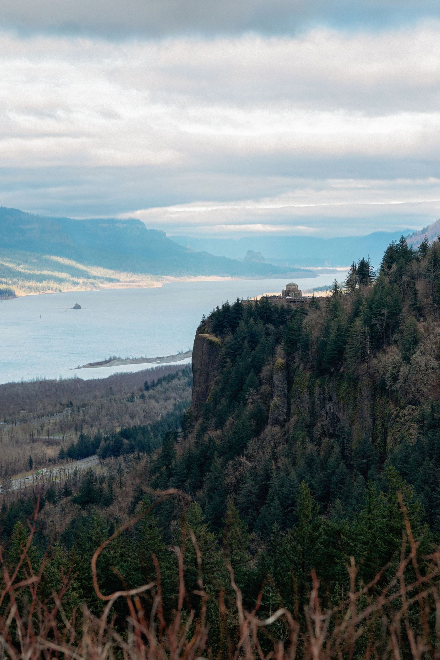 Panoramic view of evergreen forests and mountains overlooking a scenic coastline on a cloudy day.